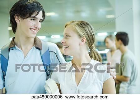 Two students standing together, smiling at each other, one's arm around the other's shoulder View Large Photo Image Stock Photograph - Two students standing together, smiling at each other, one's arm around the other's shoulder. Fotosearch