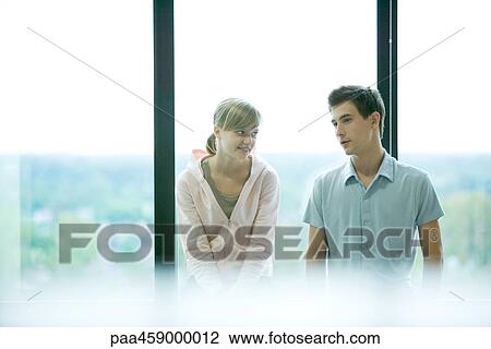 Stock Image - Two young friends chatting in front of window, selective focus. Fotosearch