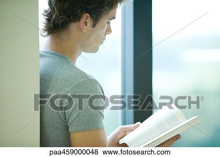 Young man reading book by window, side view View Large Photo Image Stock Photo - Young man reading book by window, side view. Fotosearch