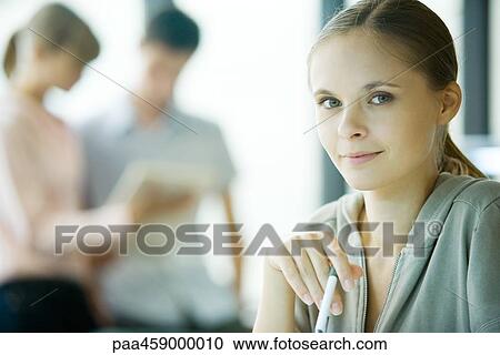 Young woman holding pen, smiling at camera View Large Photo Image Stock Image - Young woman holding pen, smiling at camera. Fotosearch