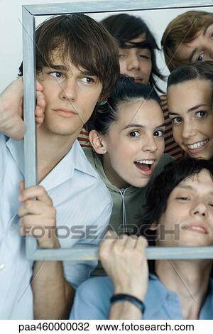 Stock Image - Group of young friends posing for photo, holding up picture frame, smiling at camera, portrait. Fotosearch