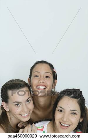 Stock Photo - Three young female friends smiling at camera, head and shoulders, portrait. Fotosearch