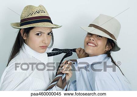 Two young female friends dressed in button down shirts, ties and hats, pulling on each other's ties, portrait View Large Photo Image Stock Photography - Two young female friends dressed in button down shirts, ties and hats, pulling on each other's ties, portrait. Fotosearch
