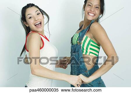 Stock Photography - Two young female friends holding hands and jumping in the air, smiling at camera, portrait. Fotosearch