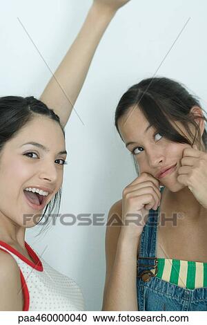 Two young female friends, one shouting with arm up, the other pulling on cheeks, looking up, portrait View Large Photo Image Stock Image - Two young female friends, one shouting with arm up, the other pulling on cheeks, looking up, portrait. Fotosearch