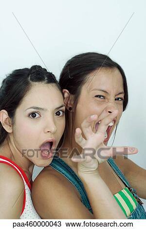 Stock Image - Two young female friends, one snarling at camera, the other with mouth open, portrait. Fotosearch