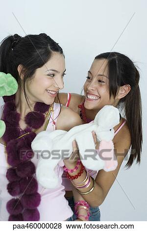 Stock Photo - Two young female friends with stuffed animals, smiling at each other, portrait. Fotosearch