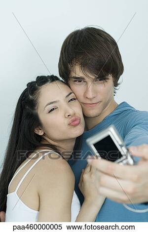 Stock Photography - Young couple posing for photo, man holding out digital camera, portrait. Fotosearch