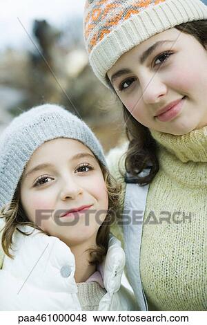 Stock Photo - Two sisters smiling at camera, wearing knit hats, portrait. Fotosearch