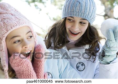 Stock Photography - Two teenage girls smiling, one holding up snowball, both dressed in winter clothing. Fotosearch