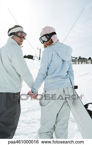 Two young friends walking, holding hands, looking over shoulders, one carrying snowboard, rear view View Large Photo Image Stock Photograph - Two young friends walking, holding hands, looking over shoulders, one carrying snowboard, rear view. Fotosearch