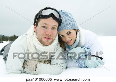 Stock Photography - Young couple lying side by side in snow, smiling at camera, portrait. Fotosearch