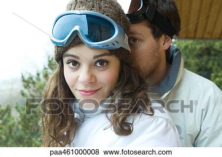 Stock Photo - Young couple standing together, female smiling at camera, boyfriend peeking from behind. Fotosearch