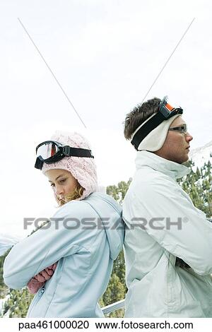 Stock Image - Young man and teen girl standing back to back, arms folded, looking away, dressed in winter clothing. Fotosearch