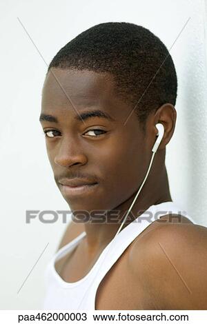 Stock Image - Male listening to earphones, looking at camera, portrait. Fotosearch