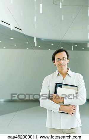 Stock Image - Man standing, smiling at camera, portrait. Fotosearch
