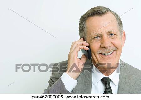 Stock Photography - Senior businessman using cell phone, smiling at camera, portrait. Fotosearch