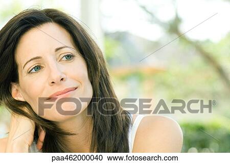 Stock Image - Woman smiling, holding head, looking away, portrait. Fotosearch