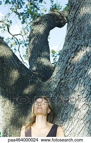 Blonde woman leaning against tree, eyes closed, low angle view View Large Photo Image Picture - Blonde woman leaning against tree, eyes closed, low angle view. Fotosearch
