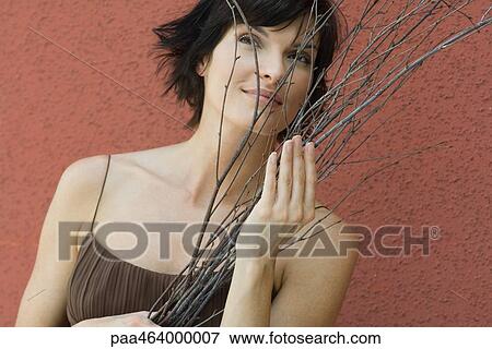 Brunette woman holding bundle of bare branches, red wall in background, head and shoulders View Large Photo Image Stock Photo - Brunette woman holding bundle of bare branches, red wall in background, head and shoulders. Fotosearch