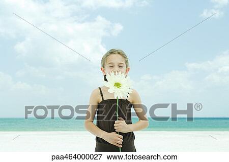 Girl holding up flower, eyes closed, standing on beach, waist up View Large Photo Image Stock Photo - Girl holding up flower, eyes closed, standing on beach, waist up. Fotosearch