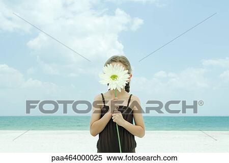 Girl holding up flower in front of face, standing on beach, waist up View Large Photo Image Stock Photography - Girl holding up flower in front of face, standing on beach, waist up. Fotosearch