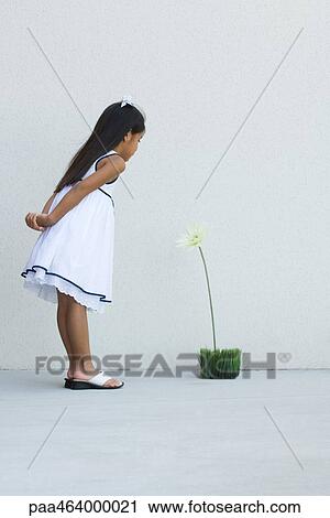 Stock Image - Girl in sundress, leaning forward, looking at flower, side view. Fotosearch