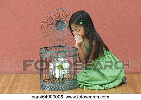 Stock Photography - Girl kneeling on floor, whispering to flower in through open top of birdcage. Fotosearch