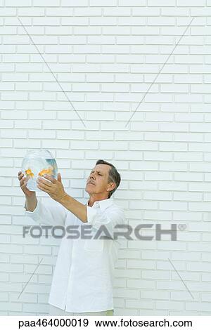 Man holding up goldfish bowl, standing in front of white brick wall, waist up View Large Photo Image Stock Photo - Man holding up goldfish bowl, standing in front of white brick wall, waist up. Fotosearch