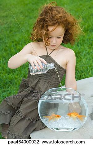 Stock Image - Redheaded little girl pouring bottled water into goldfish bowl. Fotosearch