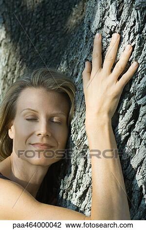 Stock Image - Woman hugging tree, eyes closed, smiling, head and shoulders. Fotosearch