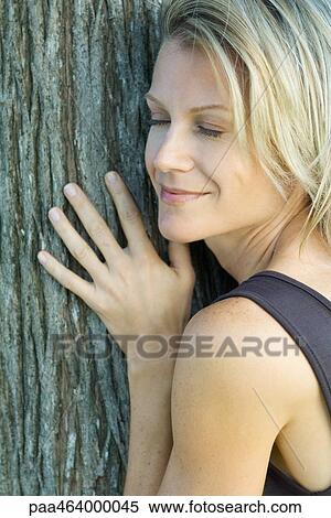 Stock Photography - Woman leaning against tree trunk, eyes closed, smiling, cropped view, full frame. Fotosearch