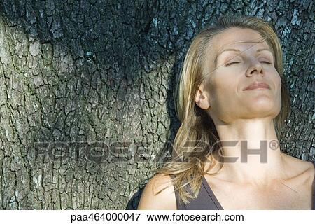 Woman leaning back against tree trunk, head and shoulders View Large Photo Image Stock Photo - Woman leaning back against tree trunk, head and shoulders. Fotosearch