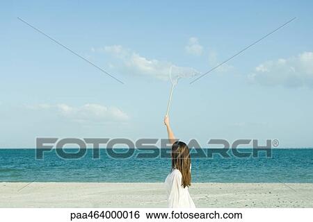 Woman on beach catching clouds with butterfly net, rear view, optical illusion View Large Photo Image Stock Photograph - Woman on beach catching clouds with butterfly net, rear view, optical illusion. Fotosearch