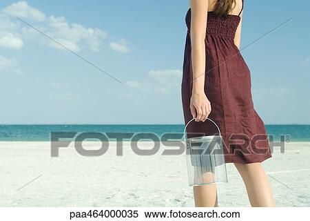 Stock Photography - Woman standing on beach, holding bucket, cropped, rear view. Fotosearch