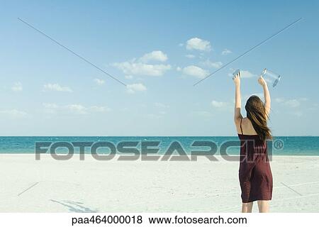 Woman standing on beach, holding up clear container, rear view View Large Photo Image Stock Photo - Woman standing on beach, holding up clear container, rear view. Fotosearch