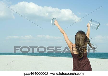Woman standing on beach, rear view, holding up clear container, catching clouds, optical illusion View Large Photo Image Stock Image - Woman standing on beach, rear view, holding up clear container, catching clouds, optical illusion. Fotosearch