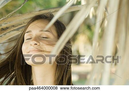 Stock Photo - Woman surrounded by dry foliage, eyes closed, hair blowing in wind, close-up. Fotosearch
