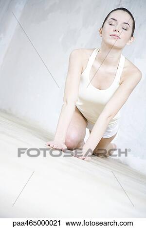 Stock Image - Woman crouching, stretching, eyes closed. Fotosearch