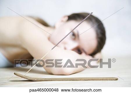 Woman lying on stomach, head resting on arms, looking at camera, incense in foreground View Large Photo Image Stock Photo - Woman lying on stomach, head resting on arms, looking at camera, incense in foreground. Fotosearch