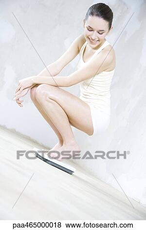 Young woman crouching on bathroom scale, looking down, smiling View Large Photo Image Stock Photo - Young woman crouching on bathroom scale, looking down, smiling. Fotosearch
