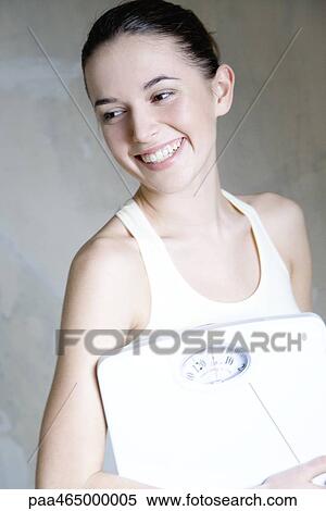 Young woman holding bathroom scale, smiling, portrait View Large Photo Image Stock Photography - Young woman holding bathroom scale, smiling, portrait. Fotosearch
