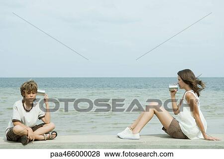 Boy and teen sister sitting next to water, talking to each other through tin can phone View Large Photo Image Stock Photo - Boy and teen sister sitting next to water, talking to each other through tin can phone. Fotosearch