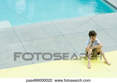 Boy sitting on the ground next to swimming pool, using cell phone View Large Photo Image Stock Image - Boy sitting on the ground next to swimming pool, using cell phone. Fotosearch