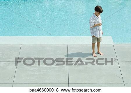 Boy standing by swimming pool, looking at cell phone, high angle view View Large Photo Image Stock Photo - Boy standing by swimming pool, looking at cell phone, high angle view. Fotosearch