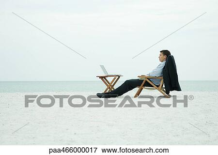 Businessman sitting with laptop computer on beach, eyes closed View Large Photo Image Stock Photo - Businessman sitting with laptop computer on beach, eyes closed. Fotosearch