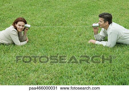 Couple lying on the ground, talking to each other through tin can phone View Large Photo Image Stock Image - Couple lying on the ground, talking to each other through tin can phone. Fotosearch