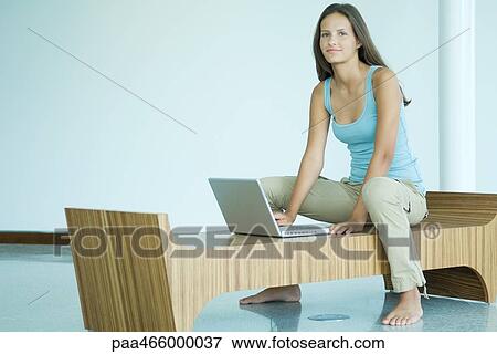 Teenage girl sitting on bench, using laptop computer, smiling at camera View Large Photo Image Stock Photo - Teenage girl sitting on bench, using laptop computer, smiling at camera. Fotosearch