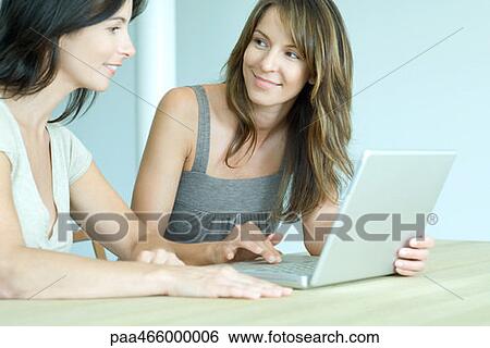 Two women using laptop computer together, smiling View Large Photo Image Stock Photograph - Two women using laptop computer together, smiling. Fotosearch
