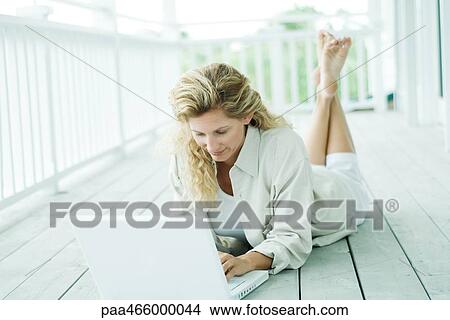 Picture - Woman lying on stomach on deck, using laptop, looking down. Fotosearch